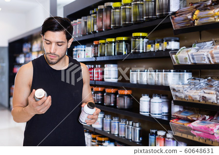 Serious young muscular man choosing sport nutrition products in shop Serious young muscular man choosing sport nutrition products in shop 60648631