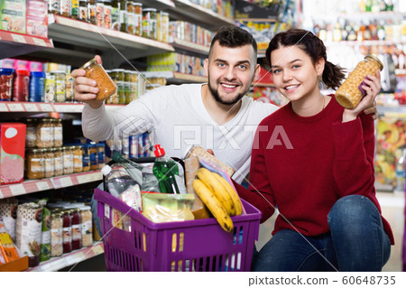 Couple standing near shelves with canned goods at store Couple standing near shelves with canned goods at store 60648735