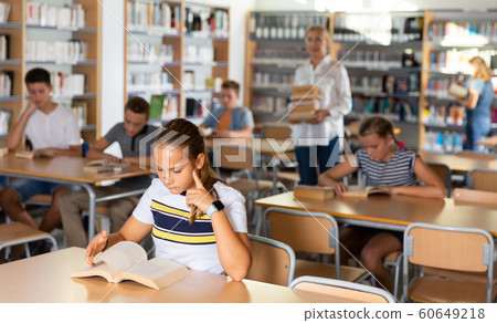 Schoolgirl preparing for lesson in ibrary, reading textbooks Schoolgirl preparing for lesson in ibrary, reading textbooks 60649218