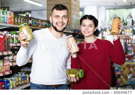 Couple standing near shelves with canned goods at store Couple standing near shelves with canned goods at store 60649677