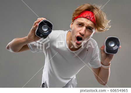 Cheeky blond guy with two portable speakers on a gray background Cheeky blond guy with two portable speakers on a gray background 60654965