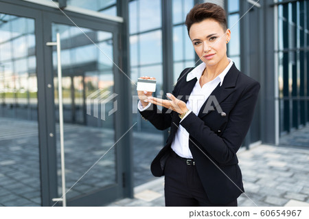 Caucasian woman in office clothes holds a credit card and waits colleague near the office building Caucasian woman in office clothes holds a credit card and waits colleague near the office building 60654967