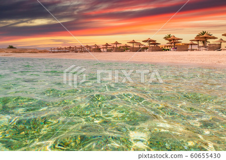 Sunset at the beach with palm trees, parasols and sunbeds. Sunset at the beach with palm trees, parasols and sunbeds. 60655430