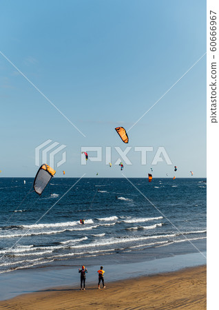 Many colorful kites on beach and kite surfers riding waves during windy day Many colorful kites on beach and kite surfers riding waves during windy day 60666967