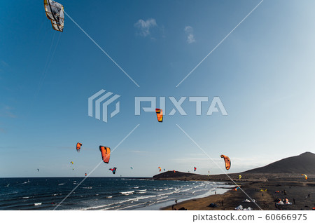 Many colorful kites on beach and kite surfers riding waves during windy day Many colorful kites on beach and kite surfers riding waves during windy day 60666975