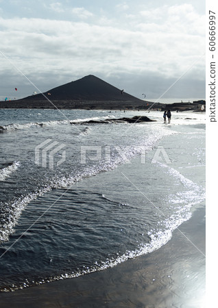 Many colorful kites on beach and kite surfers riding waves during windy day 60666997