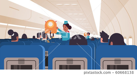stewardess explaining for passengers how to use jacket life vest in emergency situation african american flight attendants safety demonstration concept modern airplane board interior horizontal 60668138