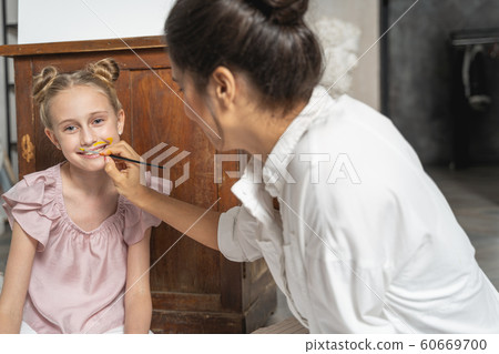 Caucasian woman painting face of little girl indoors Caucasian woman painting face of little girl indoors 60669700