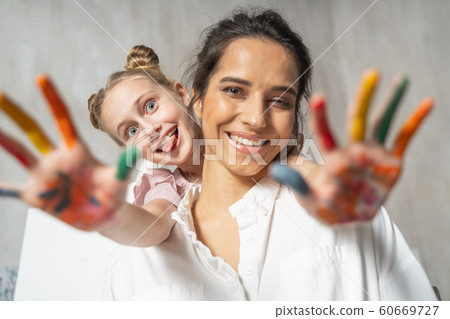 Little pretty daughter with painted palms having fun with her mum Little pretty daughter with painted palms having fun with her mum 60669727