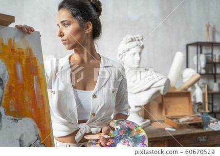 Calm concentrated female artist posing near easel Calm concentrated female artist posing near easel 60670529