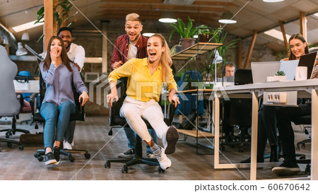 Office fun. Joyful coworkers enjoying office chair race Office fun. Joyful coworkers enjoying office chair race 60670642