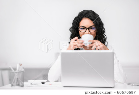 Latin woman drinking coffee and looking at laptop 60670697