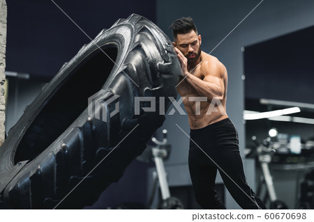 Shirtless muscular guy flipping huge tire at gym 60670698