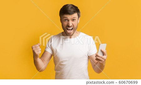 Emotional man holding phone shouting gesturing yes, yellow background, panorama 60670699