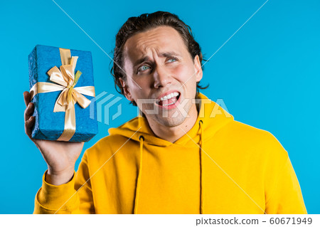 Handsome man holding gift box on blue studio background. Happy european guy received present and interested in what's inside. Handsome man holding gift box on blue studio background. Happy european guy received present and interested in what's inside. 60671949