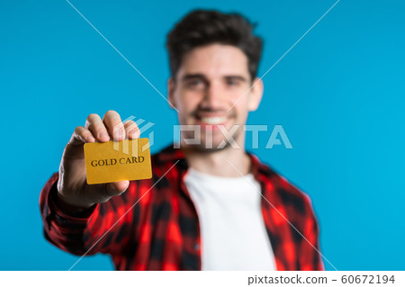 Successful man in plaid shirt showing unlimited gold credit card on blue studio background. Student, money concept Successful man in plaid shirt showing unlimited gold credit card on blue studio background. Student, money concept 60672194