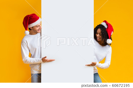 Cheerful Interracial Couple In Santa Hats Pointing At White Billboard 60672195