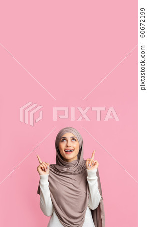 Girl in hijab pointing upwards at copy space on pink background Girl in hijab pointing upwards at copy space on pink background 60672199