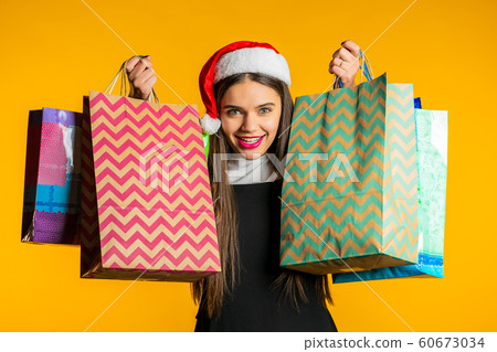 Happy young woman in Santa hat with colorful paper bags after shopping isolated on yellow studio background. Winter sale, purchases, spending money on gifts concept. Happy young woman in Santa hat with colorful paper bags after shopping isolated on yellow studio background. Winter sale, purchases, spending money on gifts concept. 60673034