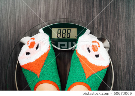 Girl standing on the scales in Christmas fun red green socks with snowman Girl standing on the scales in Christmas fun red green socks with snowman 60673069