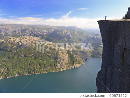 Scenic view of a hiker standing on Preikestolen (Pulpit Rock) and looking on the fjord, Norway 60673222