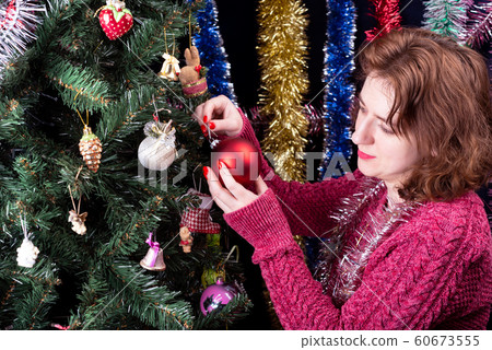 Young woman decorates a Christmas tree with green bells. Young woman decorates a Christmas tree with green bells. 60673555
