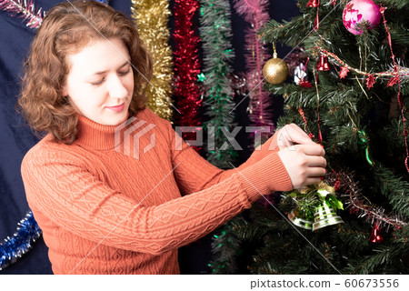 Girl decorates a Christmas tree with green bells. 60673556