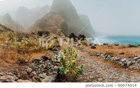 Panoramic view of stony hiking path to Ponta do Sol over amazing arid Aranhas valley with huge mountain peak and house ruins. Santo Antao Island, Cape Verde Panoramic view of stony hiking path to Ponta do Sol over amazing arid Aranhas valley with huge mountain peak and house ruins. Santo Antao Island, Cape Verde 60674014