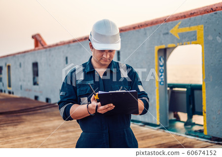 Deck Officer on deck of offshore vessel or ship , wearing PPE personal protective equipment. He fills checklist. Paperwork at sea 60674152