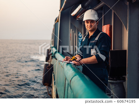 Deck Officer on deck of offshore vessel or ship , wearing PPE personal protective equipment. He fills checklist. Paperwork at sea 60674195