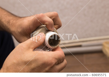 Preparing to connect the water supply. Winding the tape. Hands plumbing close-up. Preparing to connect the water supply. Winding the tape. Hands plumbing close-up. 60695571