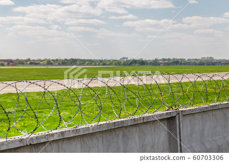 Concrete fence with barbed wire around airport airfield taxiway against blue sky on background. Freedom and security safety concept 60703306