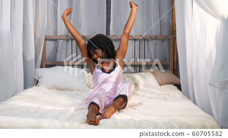 smiling African American lady wakes up and stretches on bed 60705582