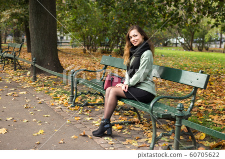Beautiful girl sitting on a bench, sunny autumn day in the park, relaxing, after work or study pretty woman 60705622