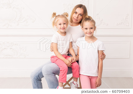 Mother who sits on chair and her daughters standing next to her pose for a photo Mother who sits on chair and her daughters standing next to her pose for a photo 60709403