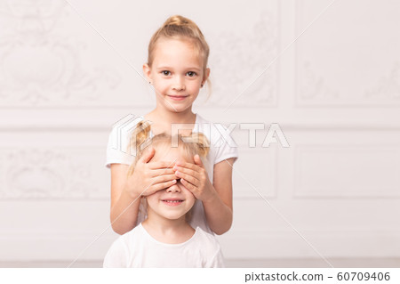 Older sister closes eyes of smiling younger one with palms 60709406