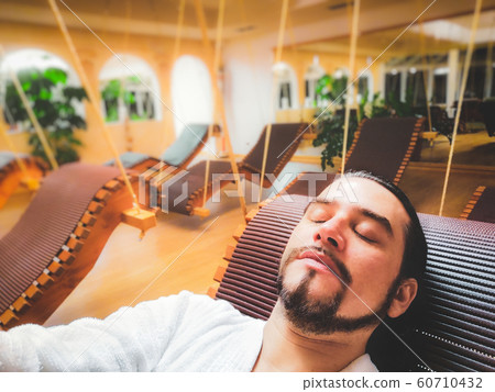 man in spa relax area on suspended deck chair alone in silence with eyes closed and bathrobe 60710432