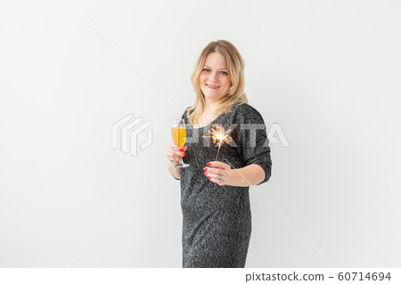 Holidays, christmas, birthday and new year concept - Woman celebrate and holds wine in a glass and sparkler over white background with copyspace 60714694