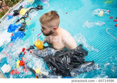 Problem of trash, plastic recycling, pollution and environmental concept - silly man swim and have fun in a polluted pool. Bottles and plastic bags float near them Problem of trash, plastic recycling, pollution and environmental concept - silly man swim and have fun in a polluted pool. Bottles and plastic bags float near them 60714996