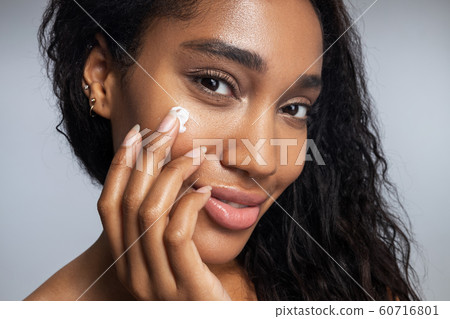 Charming Afro American woman is applying facial cream Charming Afro American woman is applying facial cream 60716801