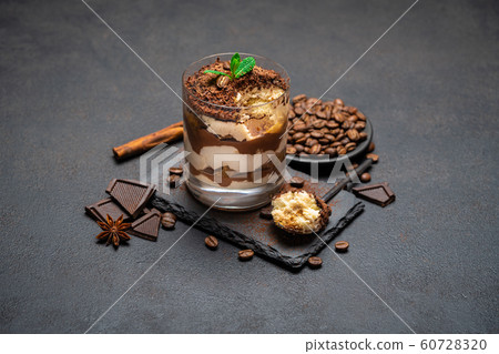 Classic tiramisu dessert in a glass cup and pieces of chocolate on stone cutting board on dark concrete background Classic tiramisu dessert in a glass cup and pieces of chocolate on stone cutting board on dark concrete background 60728320