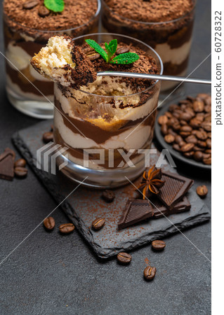 Classic tiramisu dessert in a glass cup and pieces of chocolate on stone cutting board on dark concrete background Classic tiramisu dessert in a glass cup and pieces of chocolate on stone cutting board on dark concrete background 60728322