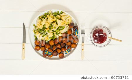 Traditional swedish meatballs (kottbullar) with cauliflower and green peas, lingonberry sauce in the white plate. Swedish flags. Swedish national food concept. Background photo 60733711