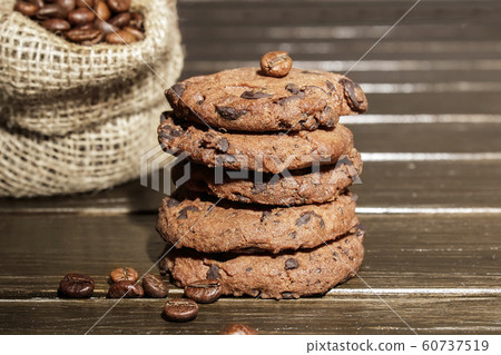Stacked chocolate chip cookies on brown wood background. Concept for a tasty snack. Sweet dessert.  Selective focus. Close up. Coffee beans. 60737519