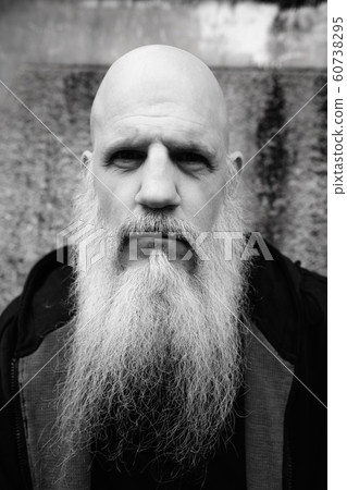 Face of mature bald man with long gray beard against concrete wall outdoors Face of mature bald man with long gray beard against concrete wall outdoors 60738295