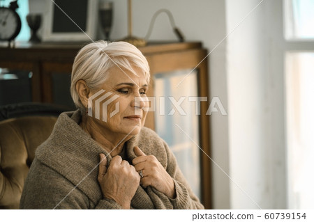 Pensive Senior Woman Wrapping Herself In A Warm Sweater Siiting On The Cosy Sofa 60739154
