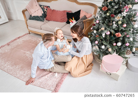 Loving family. Mom and dad hugging little daughter . Parents and baby child having fun near Christmas tree and white fireplace indoors. Merry Christmas and Happy New Year. Cheerful pretty people. 60747265