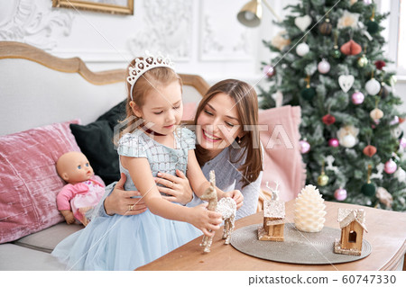 Cheerful mom embraces her cute baby daughter . Parent and little child having fun near Christmas tree indoors. Loving family Merry Christmas and Happy New Year Cheerful mom embraces her cute baby daughter . Parent and little child having fun near Christmas tree indoors. Loving family Merry Christmas and Happy New Year 60747330