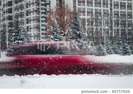 a car in motion rides along a tall building on a winter road in snow a car in motion rides along a tall building on a winter road in snow 60757688