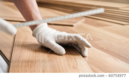 Installing laminated floor, detail on man hands in white gloves, holding measuring tape over wooden tiles 60758977